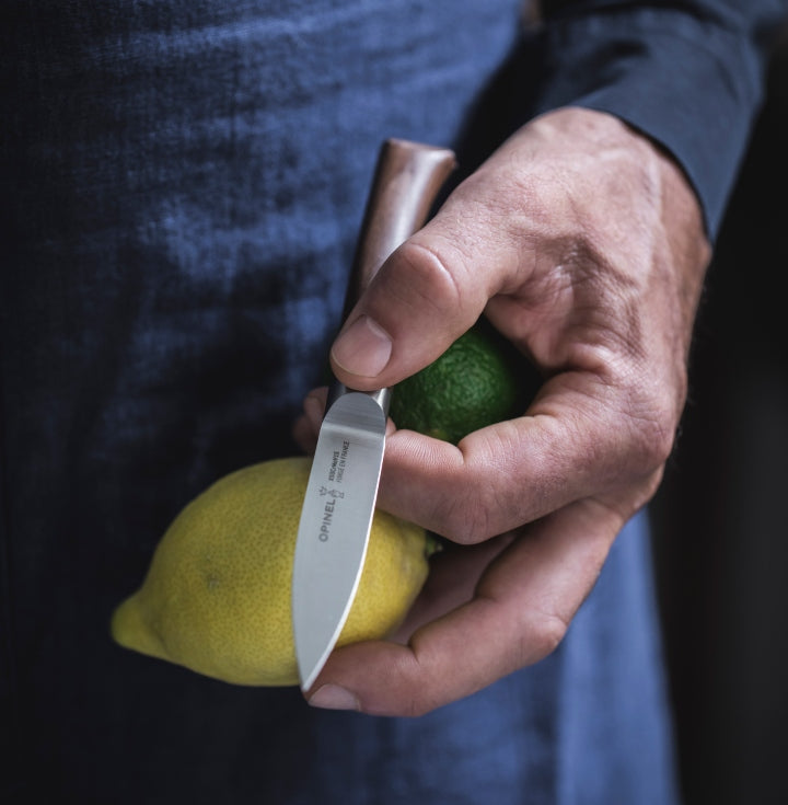image of an opinel knife in a hand of a person holding onto lemons, limes and wearing the opinel apron